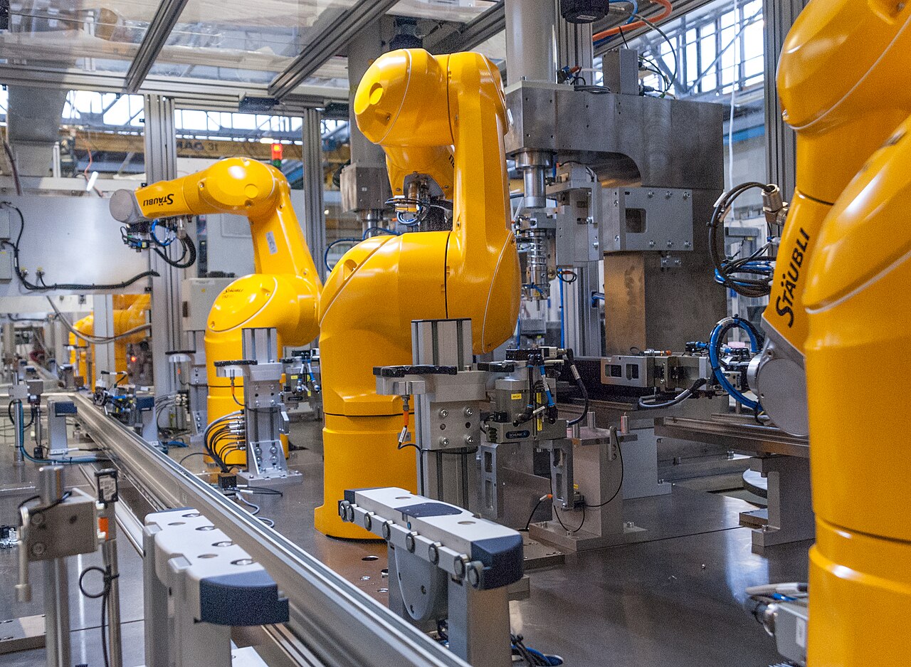 Several yellow industrial robot arms operate together along a manufacturing line.